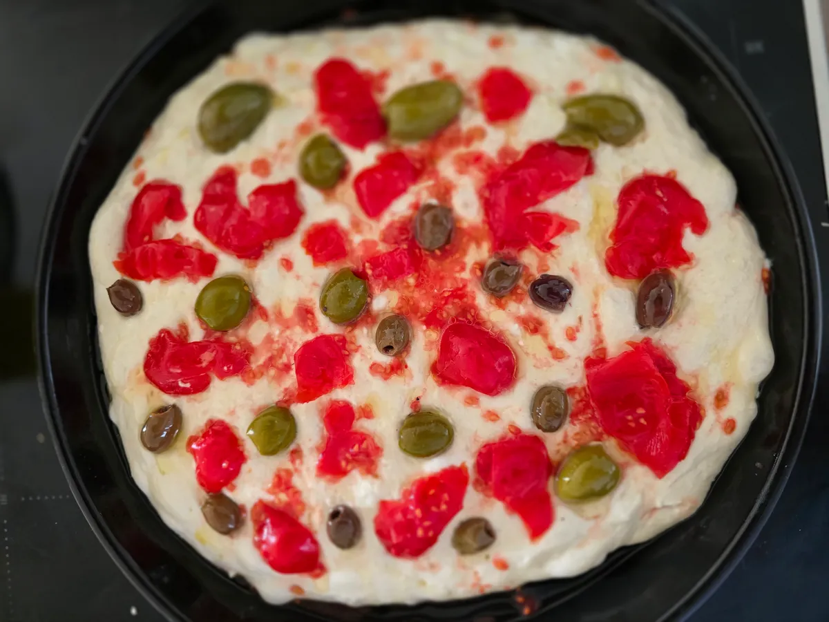 Focaccia-Teig im Blech mit Tomaten und Oliven vor dem Backen