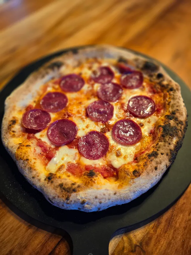 Fertig gebackene neapolitanische Pizza auf schwarzer Servierplatte — perfekter Cornicione